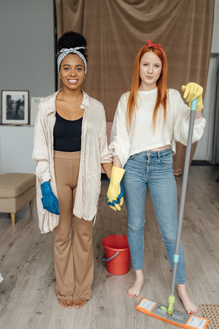 gallery-1 Two women smiling and holding hands while cleaning indoors, symbolizing teamwork.